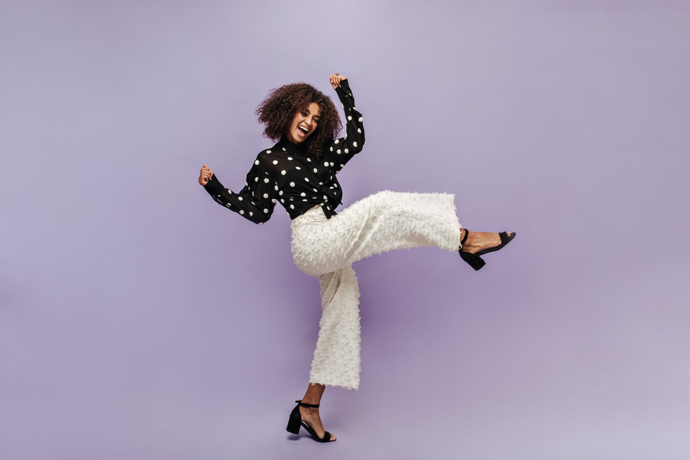 Positive Trendy Girl with Cool Hairstyle in Black Polka Dot Blouse, Unusual Pants and Modern Heels Rejoicing and Looking into Camera